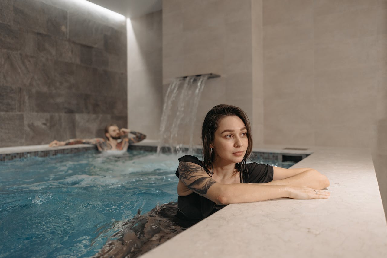 Tattooed woman and man enjoying a modern indoor pool setting, emphasizing relaxation.