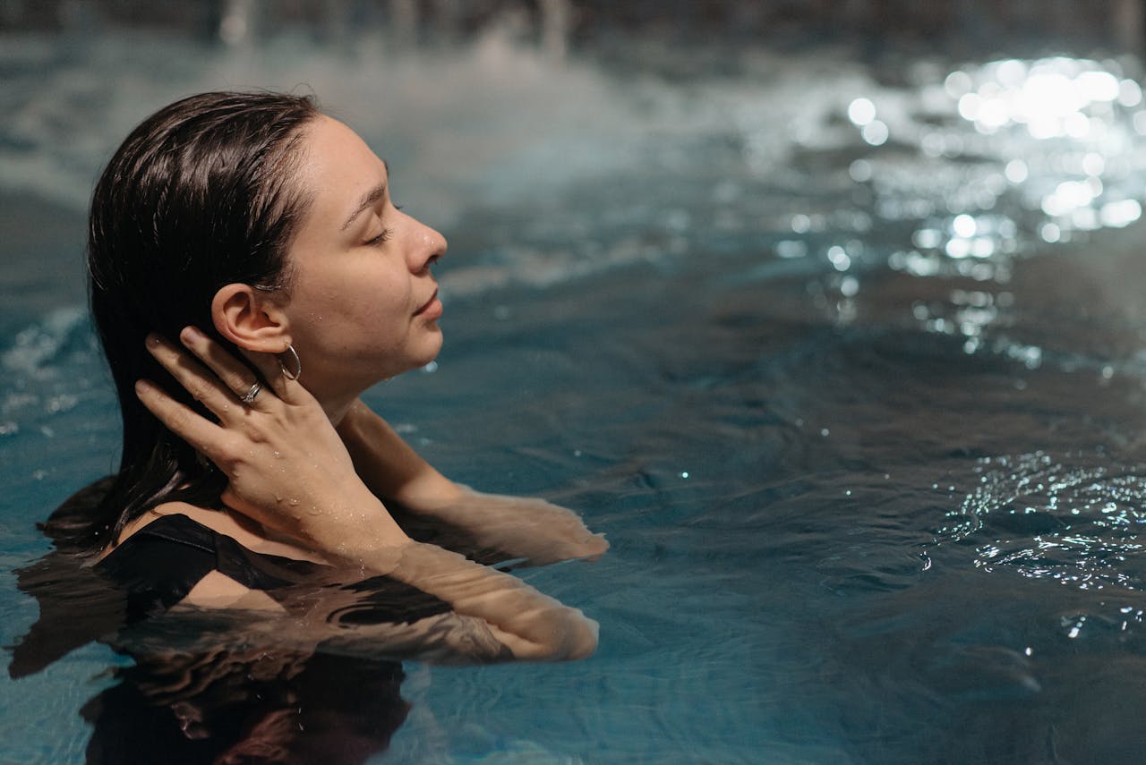 A woman relaxes with eyes closed in a nighttime swimming pool setting, enjoying tranquility.